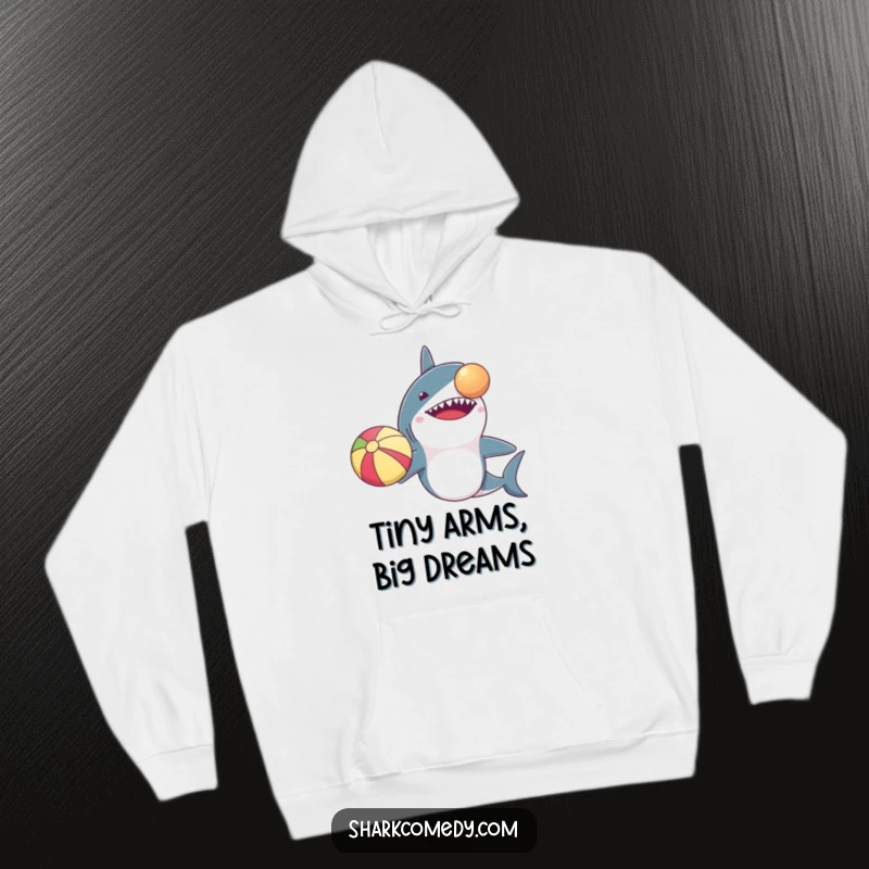 Funny hoodie design: a shark with comically small arms precariously balancing a beach ball on its nose for maximum laughs.